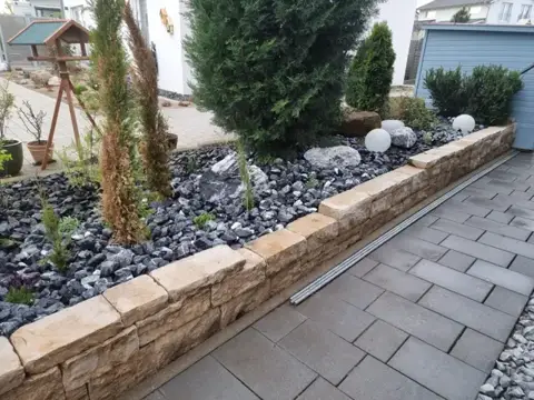 Natursteinmauer entlang einer bepflanzten Fläche